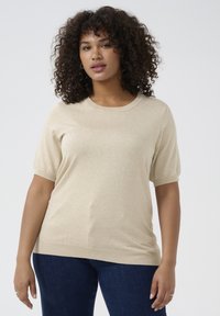 Beige short-sleeve sweater with a round neckline, soft texture, and ribbed hem. Paired with dark blue jeans.