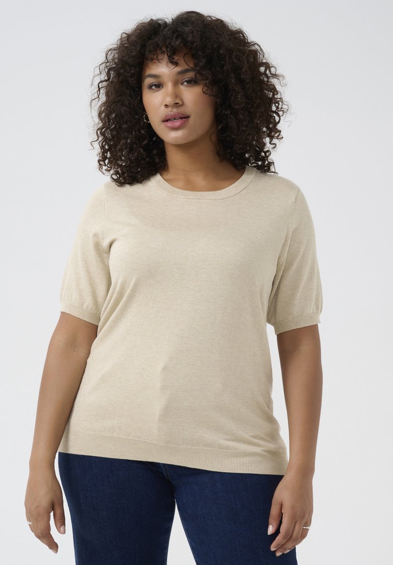 Beige short-sleeve sweater with a round neckline, soft texture, and ribbed hem. Paired with dark blue jeans.