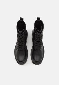 Paire de bottines noires en cuir à lacets avec fermetures éclair sur les côtés, bouts ronds et languettes de tirage, vues de dessus sur un fond blanc.