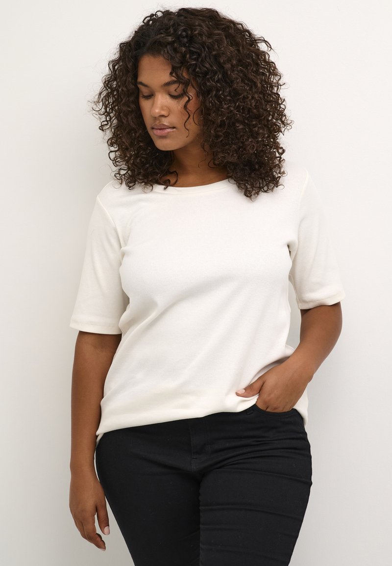 White, short-sleeve top in soft fabric with a round neckline and relaxed fit, paired with black fitted pants. Smooth texture, minimal design.