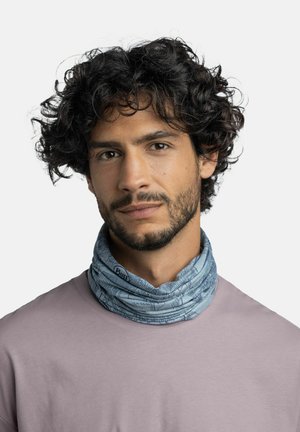 Man with curly dark hair and beard wearing a light purple shirt and a blue patterned neck gaiter against a plain background.