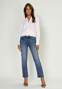 Witte blouse met gerimpelde voorkant, gecombineerd met straight-leg blauwe jeans en zwarte open teen hakken. Gladde stof en nauwkeurige pasvorm.