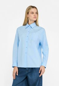 Lichtblauw knoopshirt met een kraag, lange mouwen en metallic accentdetails. Beschikt over een borstzak en een gladde, gestructureerde stof.