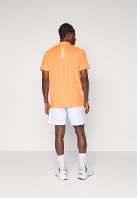 T-shirt de sport orange à manches courtes avec des rayures verticales blanches et l'inscription "BORG" dans le dos. Assorti à un short blanc et des chaussures.
