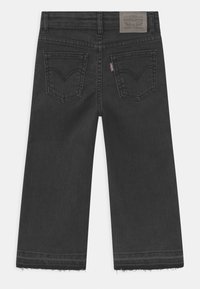 Černé denimové široké džíny s třepeným lemem, obsahující dvě zadní kapsy a hnědou koženou nášivku na pásu se detaily loga.