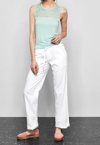 Haut sans manches en teal clair avec des détails en dentelle, associé à un pantalon large blanc et des espadrilles roses. Tissu doux, coupe décontractée.