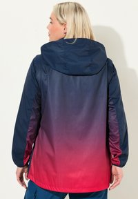Veste imperméable arborant un dégradé de bleu marine à rouge, avec capuche, manches longues et poignets élastiques, fabriquée en tissu lisse et léger.