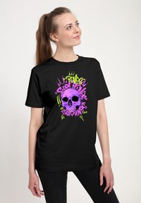 Černé tričko s výrazným grafickým motivem lebky v růžové a zelené barvě, obklopené stylizovaným textem, navržené s volným střihem a krátkými rukávy.
