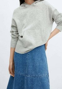 Lichtgrijze hoodie met een voorzak en een capuchon met verstelbare koord, gecombineerd met een knielange blauwdenim rok met horizontale naden.
