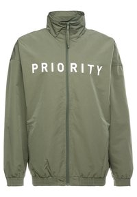 Groene lichte jas met een hoge kraag, volledige rits en elastische manchetten. Heeft "PRIORITY" in het wit op de voorkant gedrukt.