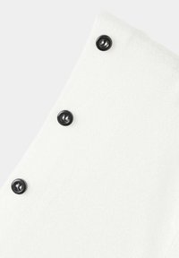 Panneau en tissu blanc avec trois boutons ronds noirs alignés en diagonale sur un fond clair.