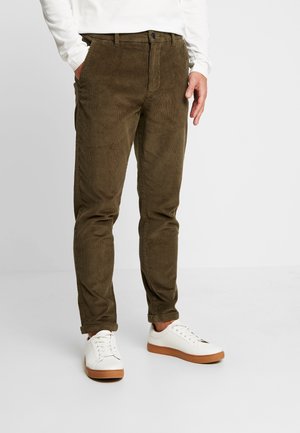 Olive green corduroy pants with a slim fit, featuring a button closure, side pockets, and cuffs rolled up, paired with white sneakers.