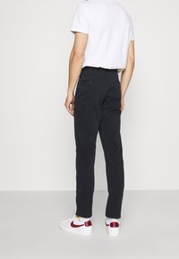 Dark navy chinos made of cotton, featuring a slim fit, standard back pockets, and paired with white sneakers with red accents.