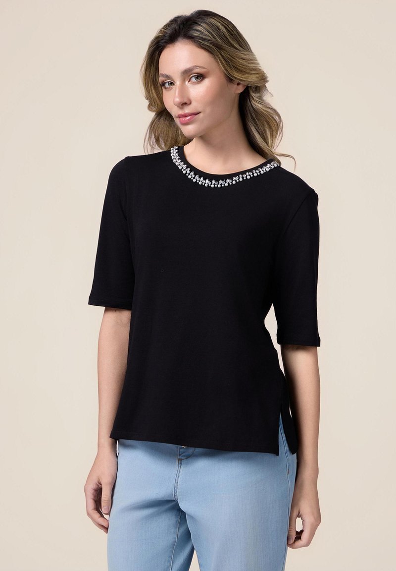 Top corto negro de manga corta con un escote redondeado adornado con un borde decorativo de cuentas plateadas, con aberturas laterales y un corte holgado.