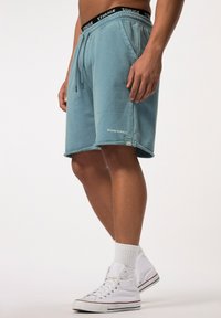 Lichtblauwe shorts met een elastische tailleband en koord, voorzien van zijzakken, merkaccenten en een raw edge zoom. Gecombineerd met witte sneakers.