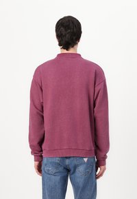 Sweatshirt bordeaux avec une coupe décontractée, col rond, poignets et ourlet côtelés. Fabriqué en matériau doux, il présente une texture unie sans motifs.