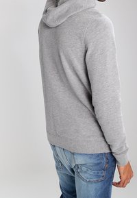 Sudadera con capucha gris hecha de un tejido suave, con un bolsillo tipo canguro y dobladillo acanalado, combinada con jeans de mezclilla azul que presentan un leve desvanecimiento.