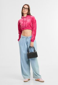 Rosa Cropped-Hoodie aus weichem Material, hellblaue weit geschnittene Jeans und eine kleine schwarze Handtasche mit silbernen Akzenten. Sneaker mit pinken und orangefarbenen Streifen.