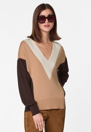 V-Ausschnitt Pullover in Beige, Creme und Braun, mit langen Ärmeln und Farbblockdesign. Glatte Textur und gerippte Bündchen. Getragen mit Sonnenbrille.
