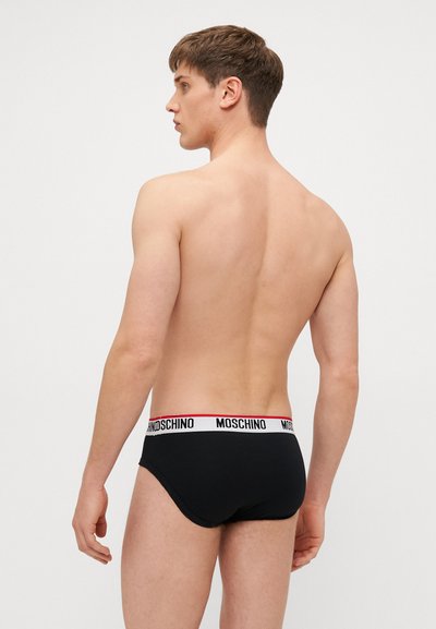 Boxers noirs en coton avec une ceinture blanche portant le logo "Moschino" en noir et rouge, vus de dos. Texture lisse.