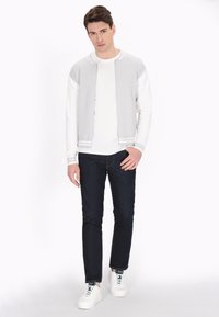 Chaqueta bomber gris con cremallera, camiseta de manga larga blanca, jeans azul marino y zapatillas blancas. La chaqueta tiene puños y cuello acanalados.