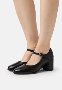 Scarpe con tacco in pelle nera, con punta arrotondata, cinturino alla caviglia e tacco a blocco. Texture liscia con un design semplice e fibbia regolabile.