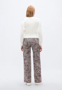 Λευκό φούτερ με εφαρμοστή μέση και ριμπ μανσέτες, συνδυασμένο με παντελόνια φαρδιά με σχέδιο λεοπάρ σε αποχρώσεις καφέ και κρεμ.