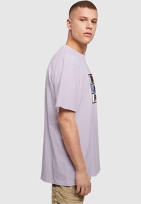 Camiseta de algodón lila con mangas cortas, escote redondo y un diseño gráfico de estampados coloridos en la parte delantera.