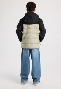 Black and light green puffer jacket with a hood, featuring a quilted design. Worn over wide blue jeans, highlighting a casual fit.