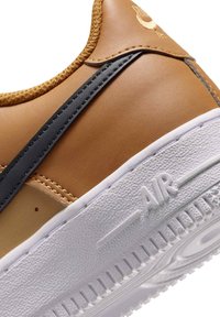 Brązowe skórzane sneakersy z teksturowaną białą podeszwą, szarym paskiem bocznym i złotymi akcentami. Charakteryzują się haftowanymi detalami oraz wytłoczonym napisem 'AIR'.