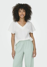 Haut blanc à col en V avec des manches courtes et évasées, associé à un pantalon élastique taille haute de couleur vert clair. Texture lisse avec une coupe décontractée.