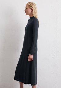 Sukienka z długim rękawem w ciemnoszarym kolorze, wykonana z miękkiego materiału; posiada falbaniasty dekolt i dół, co tworzy gładką sylwetkę.