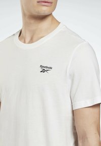 Balta kokvilnas T-krekls ar apaļo kaklu un īsām piedurknēm. Uz kreisā krūtīm izšūts melns Reebok logo. Mīksta tekstūra.