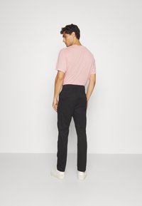 T-shirt a girocollo rosa chiaro, pantaloni neri su misura e sneakers bianche. L'outfit presenta una vestibilità slim e un design minimalista.