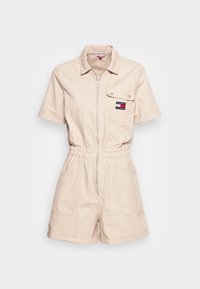 Bežový krátký overal vyrobený z bavlny, se zipem na přední straně, krátkými rukávy a náprsní kapsou s logem. Elastický pas.