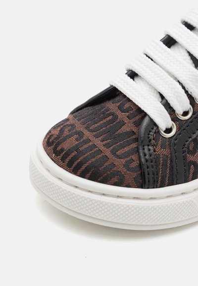 Kengūros su raišteliais su rudu raštuotu kanvoso viršumi, kuriame yra juodas tekstas, baltos raišteliai ir tekstūruotas baltas gumos padas.