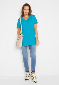 T-shirt turchese con scollatura a V, maniche corte, abbinato a jeans azzurri chiari. Presenta una borsa a tracolla beige e sneakers chunky multicolore.