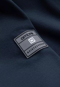 Tessuto navy con un patch in gomma nera testurizzata che presenta la parola "onlore" e "quintessence" in rilievo.