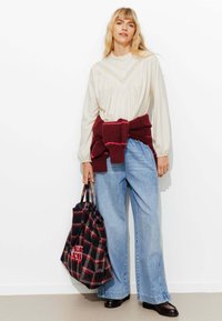 Blouse en tricot crème avec un col à volants, assortie à un jean large bleu clair. Un pull bordeaux est noué à la taille ; un sac à carreaux est inclus.