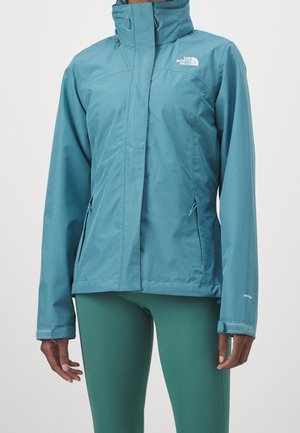 Wodoodporna kurtka North Face w kolorze teal z wysokim kołnierzem, przednim zamkiem krytym patką przeciwdeszczową, zapinanymi na zamek bocznymi kieszeniami oraz zapięciami na rzepy przy mankietach.