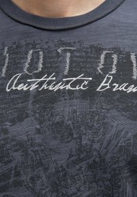 Kurzärmliges dunkelgraues T-Shirt mit einem strukturierten Grafikdesign und gesticktem Text "Authentic Brand" in Weiß. Runder Ausschnitt.