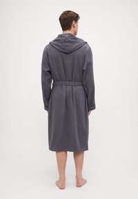 Grå frottébadekåpe med hette, lange ermer og belte i midjen. Har en teksturert stoff og kne-lengde design.