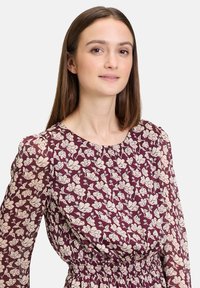 Blumenmusterkleid mit burgunderfarbenem Hintergrund und cremefarbenen Blumenmustern, elastischem Bund und langen Puffärmeln. Leichter, strukturierter Stoff.