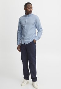 Light blue button-up shirt, navy pants, and white sneakers. Smooth fabric, tailored fit, classic collar, and straight leg design.