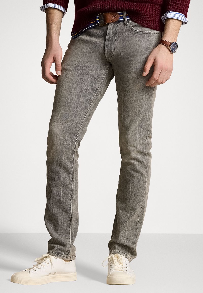 Grå denimjeans med slim fit, med falmet tekstur, fem lommer og et brunt lærbelte med striper. Kombinert med hvite sneakers.