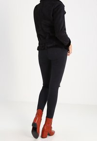 Svart fuskmockajacka med fodrad krage och figursydd design, tillsammans med svarta skinny jeans och röda kraftiga klackstövlar.