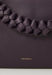 Purple leather handbag featuring a braided handle and embossed logo in gold. Textured surface with a slightly pebbled finish.