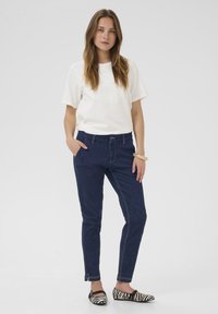 T-shirt blanc à manches courtes avec un graphique texturé, associé à un jean ajusté bleu foncé et des chaussures plates rayées noir et blanc.