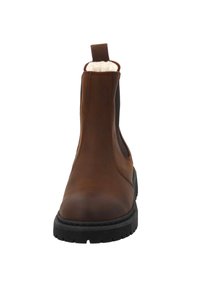 Brązowe skórzane botki Chelsea z elastycznymi panelami bocznymi, pętelką do zakładania i teksturowaną czarną gumową podeszwą. Miękka, futrzana podszewka widoczna na górze.