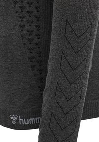 Ciemnoszara tkanina z długim rękawem z czarnymi wzorami w zygzak na rękawie i małymi powtarzającymi się motywami pszczół w pobliżu mankietu oraz tekstem logo "hummel".